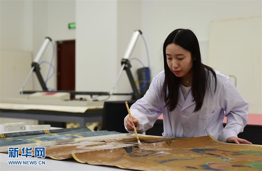 5月17日，文物修复技师张芯语在去除画卷上的附着物。